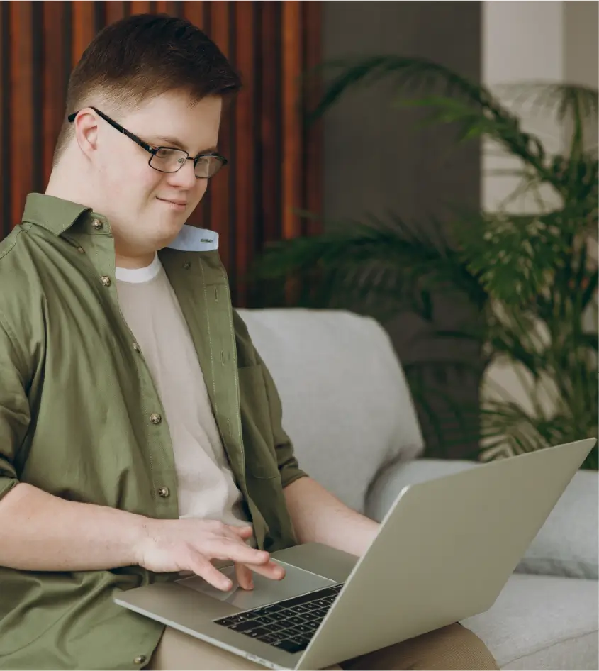A neurodivergent male student working on his laptop on a sofa.