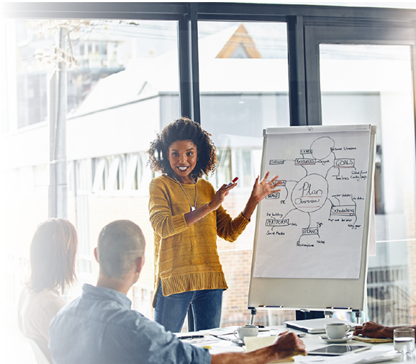 A confident African-American woman explains a plan on a whiteboard to a diverse group of professional.