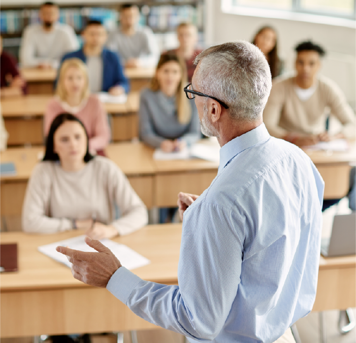 A male professor lectures to a class of diverse students.