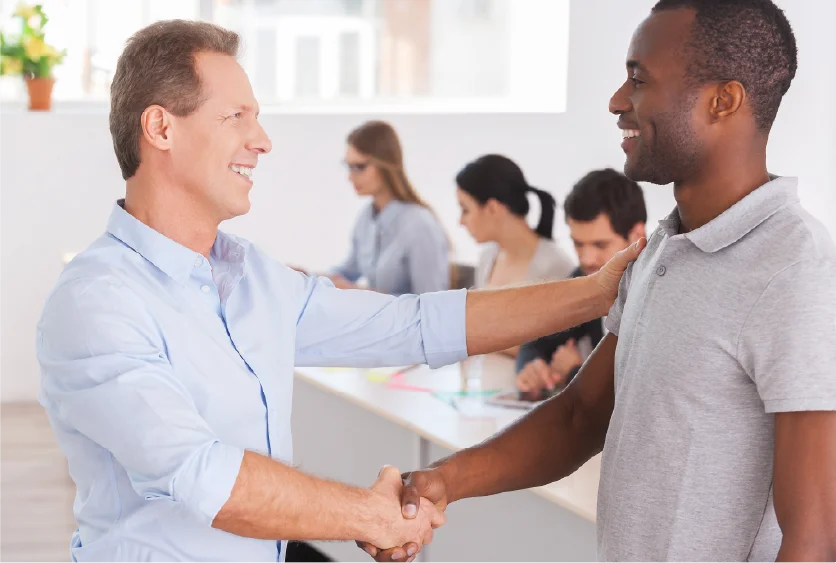 Two men smiling and shaking hands in a professional setting.