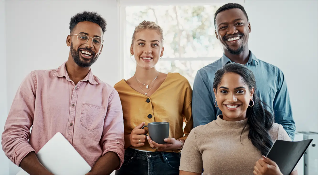 Four diverse students smiling together, holding laptops and coffee.