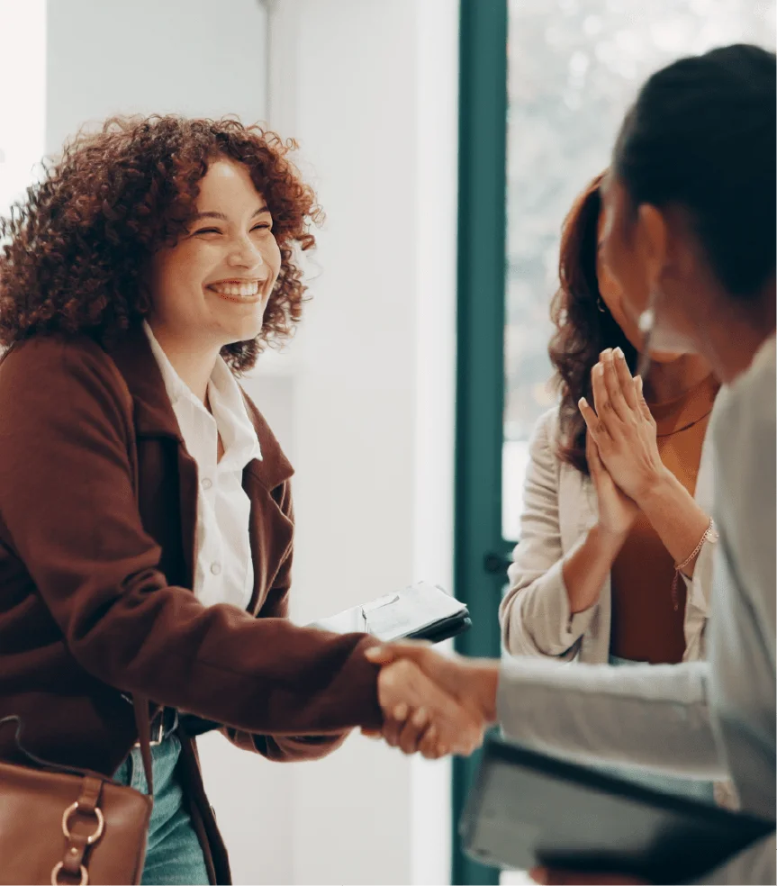A smiling student warmly shakes her hands in a friendly, professional greeting.