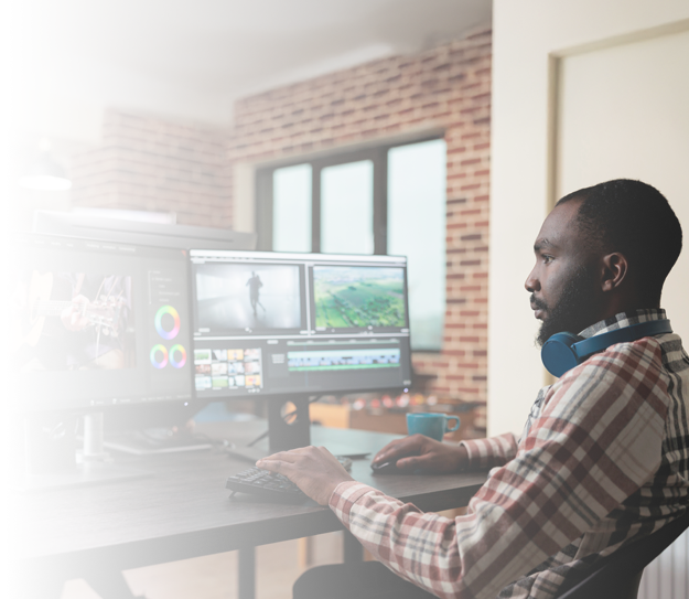 A man working editing a video on one screen while being on a conference call on another screen.